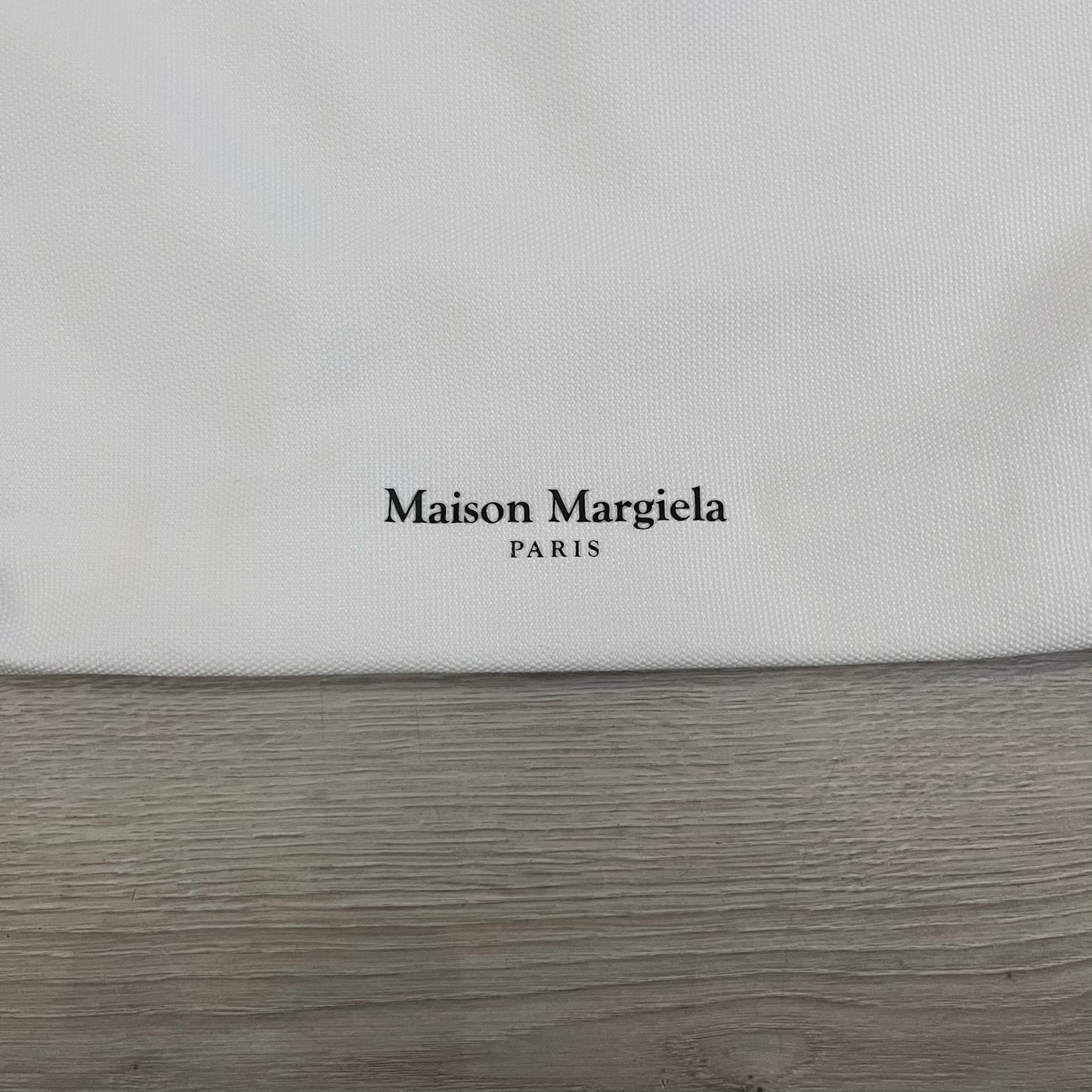 Maison Margiela Replica Tote Bag in off-white with a textured finish inspired by natural jute. Features “Replica” fragrances patch on one side, an interior slip pocket, and small “Maison Margiela Paris” text on the other side. Made in Paris, versatile for daily errands, work, or casual outings.