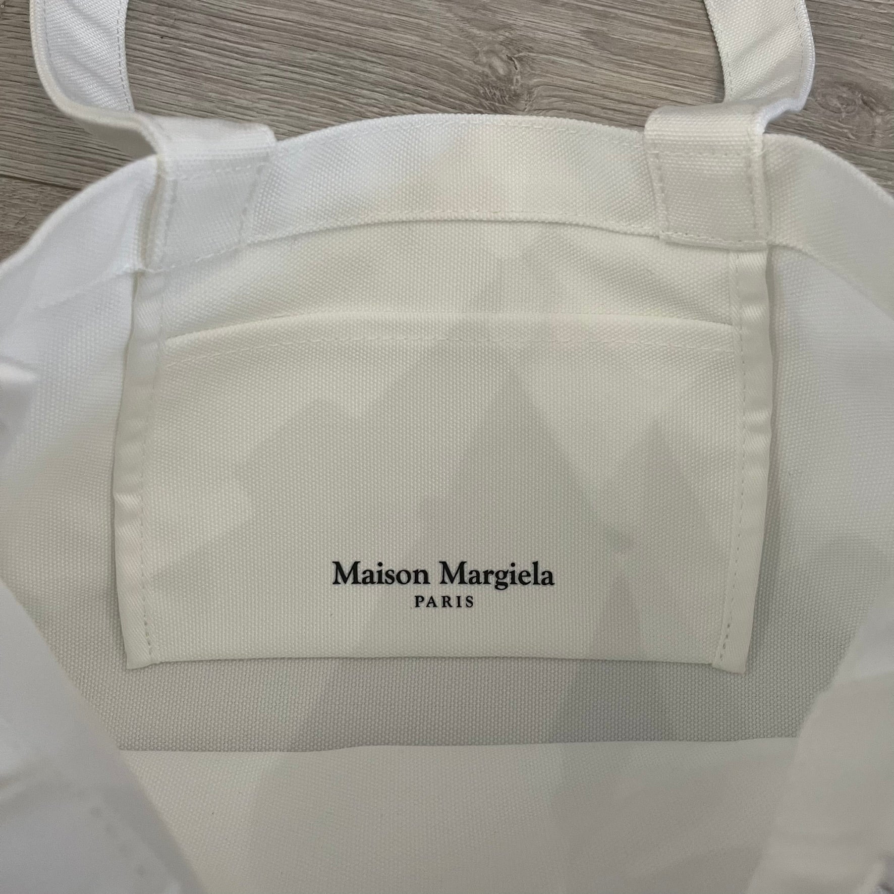 Maison Margiela Replica Tote Bag in off-white with a textured finish inspired by natural jute. Features “Replica” fragrances patch on one side, an interior slip pocket, and small “Maison Margiela Paris” text on the other side. Made in Paris, versatile for daily errands, work, or casual outings.