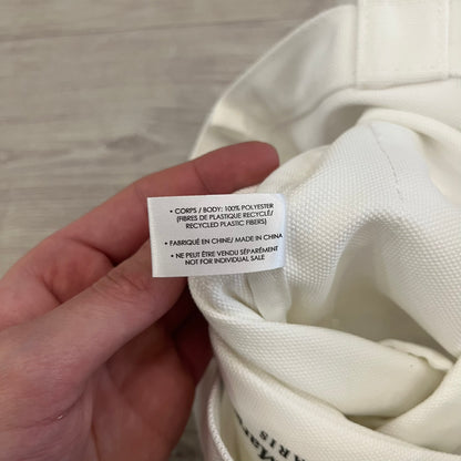 Maison Margiela Replica Tote Bag in off-white with a textured finish inspired by natural jute. Features “Replica” fragrances patch on one side, an interior slip pocket, and small “Maison Margiela Paris” text on the other side. Made in Paris, versatile for daily errands, work, or casual outings.