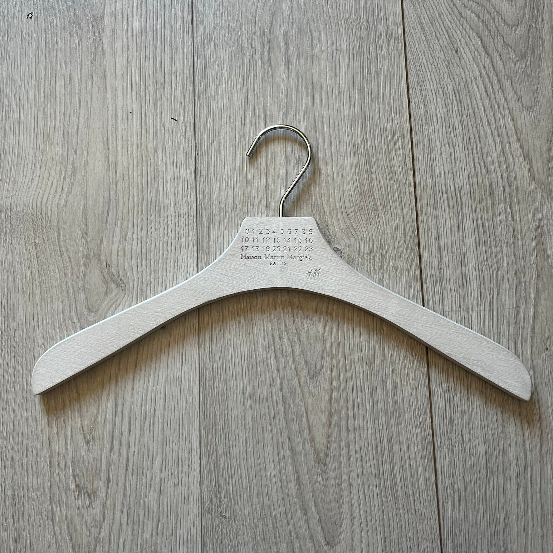 Maison Margiela x H&amp;M 2012 clothing hanger in a white-washed wood finish. Features a carved Margiela and H&amp;M logo with a clean, classic silhouette. Ideal for displaying tees, hoodies, or jackets with a touch of designer minimalism.