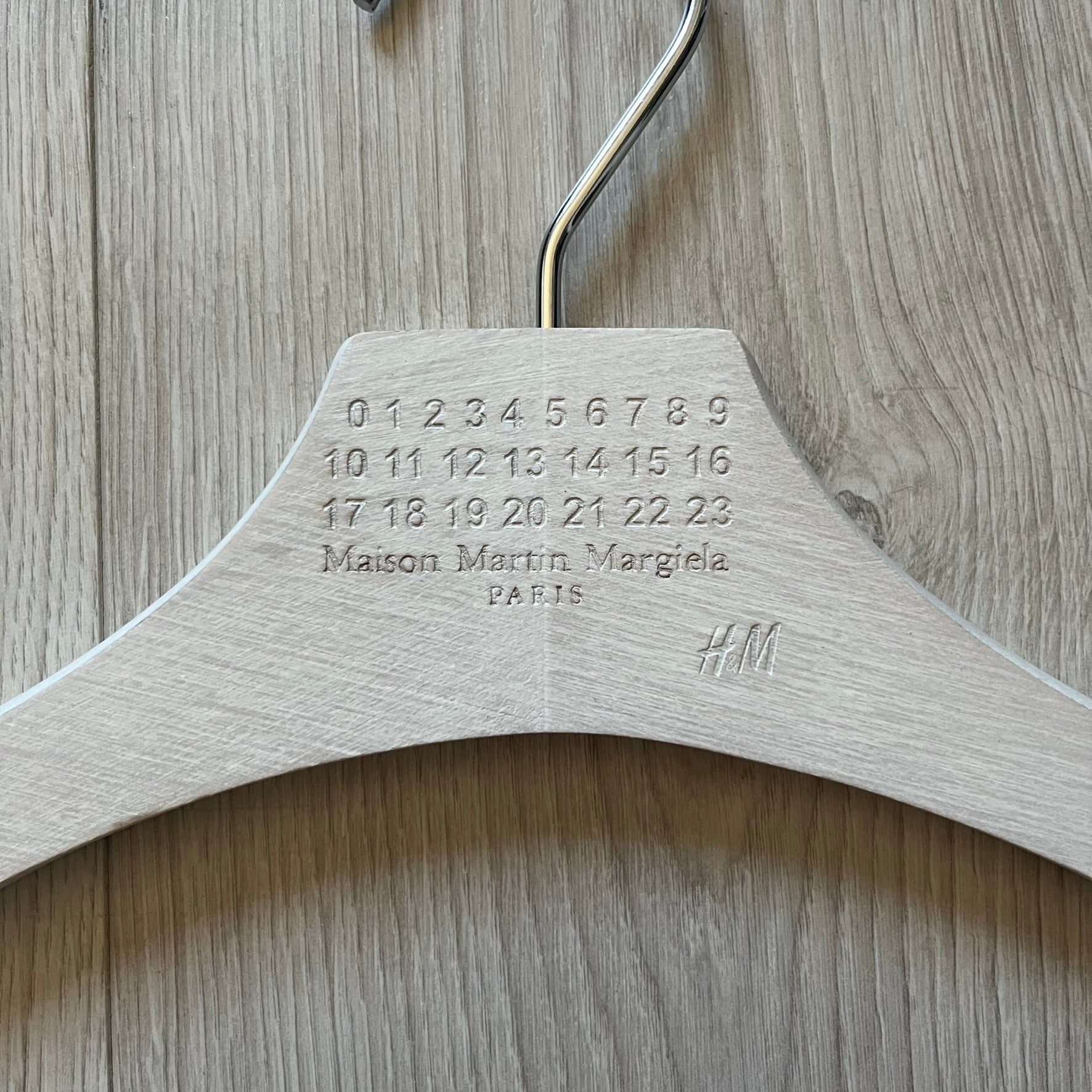 Maison Margiela x H&amp;M 2012 clothing hanger in a white-washed wood finish. Features a carved Margiela and H&amp;M logo with a clean, classic silhouette. Ideal for displaying tees, hoodies, or jackets with a touch of designer minimalism.