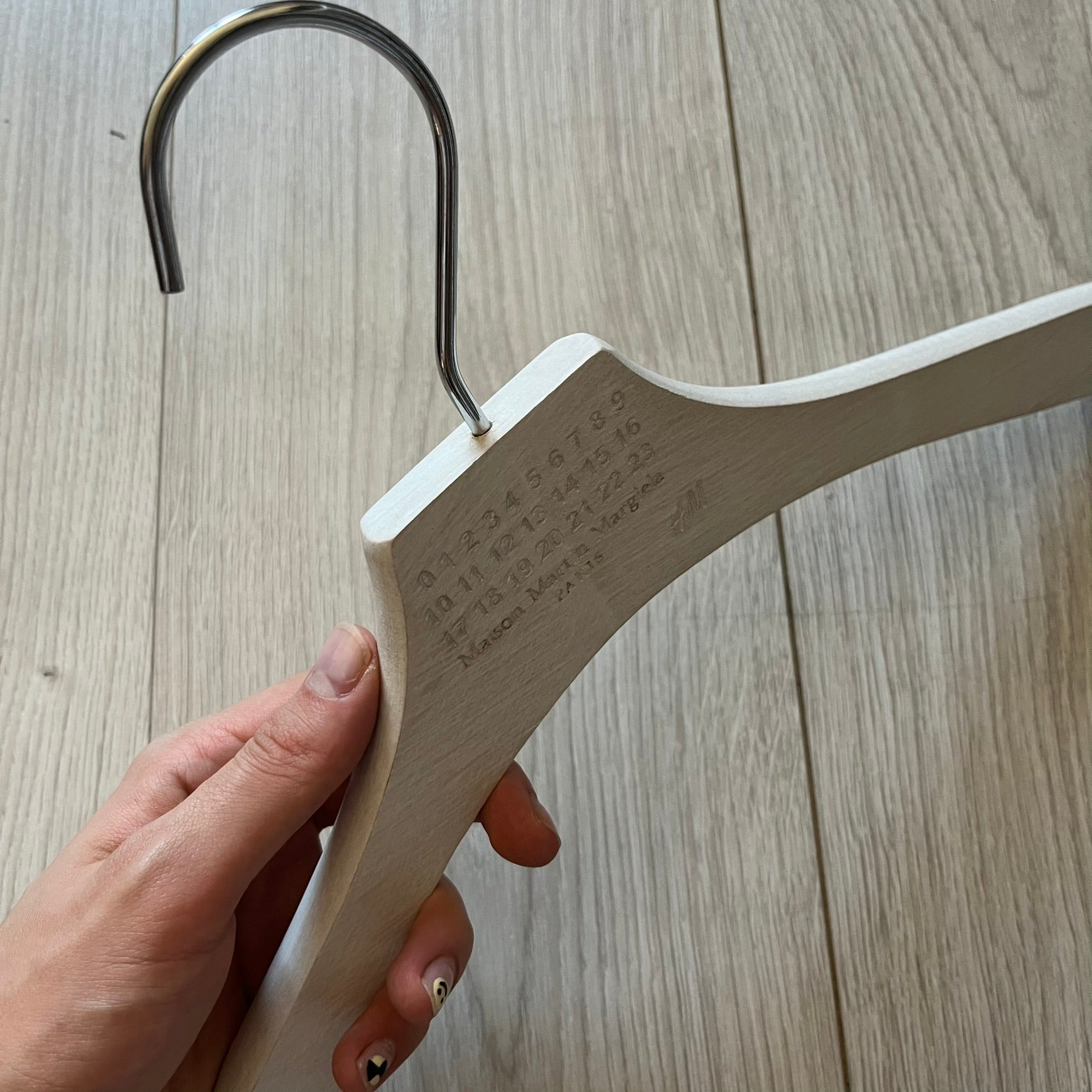 Maison Margiela x H&amp;M 2012 clothing hanger in a white-washed wood finish. Features a carved Margiela and H&amp;M logo with a clean, classic silhouette. Ideal for displaying tees, hoodies, or jackets with a touch of designer minimalism.