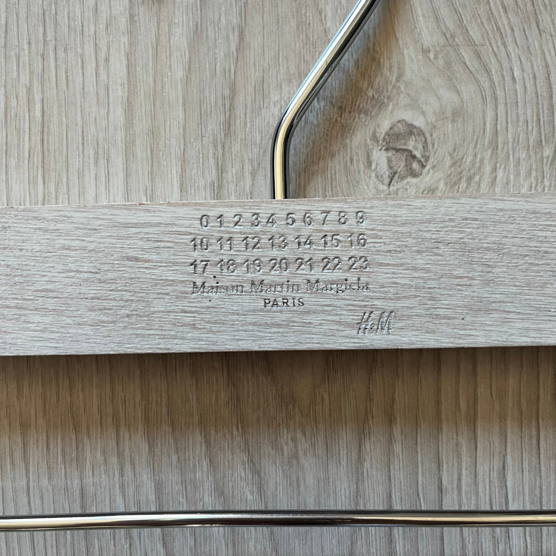 Maison Margiela x H&amp;M 2012 hanger in a white-washed wood finish with engraved logos. Features a straight wooden bar with metal clips, perfect for hanging pants, skirts, or shorts. A rare, functional collectible from this iconic collaboration.