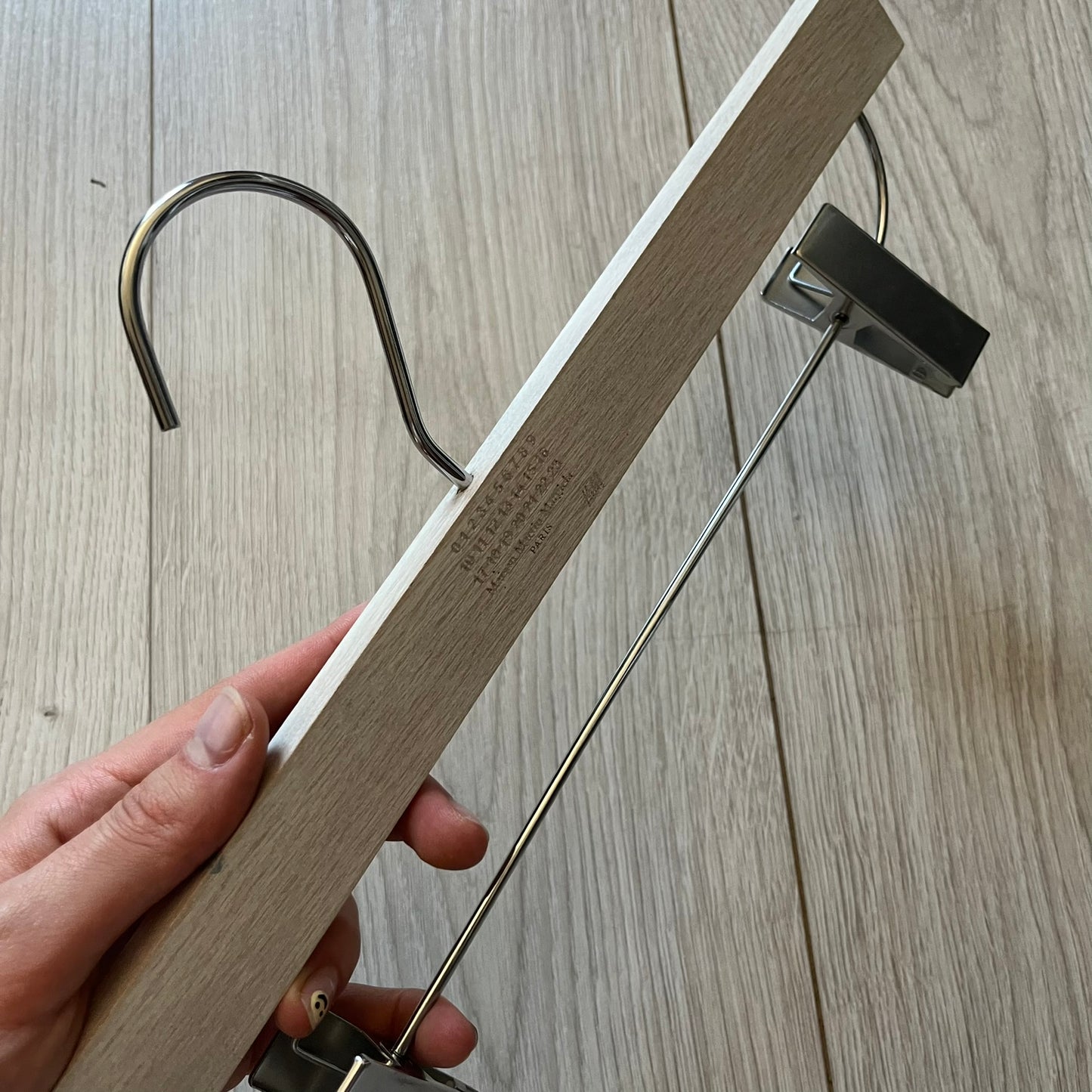 Maison Margiela x H&amp;M 2012 hanger in a white-washed wood finish with engraved logos. Features a straight wooden bar with metal clips, perfect for hanging pants, skirts, or shorts. A rare, functional collectible from this iconic collaboration.
