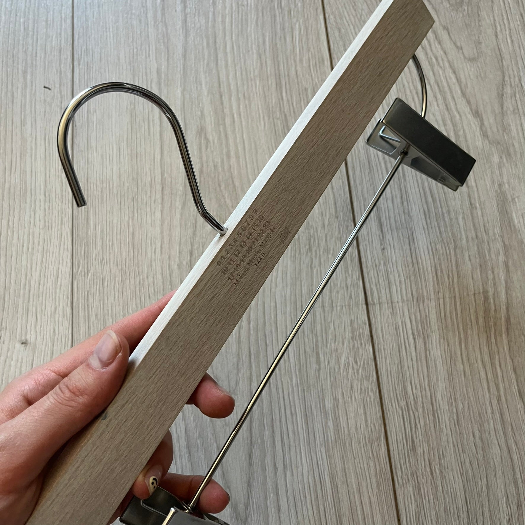 Maison Margiela x H&amp;M 2012 hanger in a white-washed wood finish with engraved logos. Features a straight wooden bar with metal clips, perfect for hanging pants, skirts, or shorts. A rare, functional collectible from this iconic collaboration.