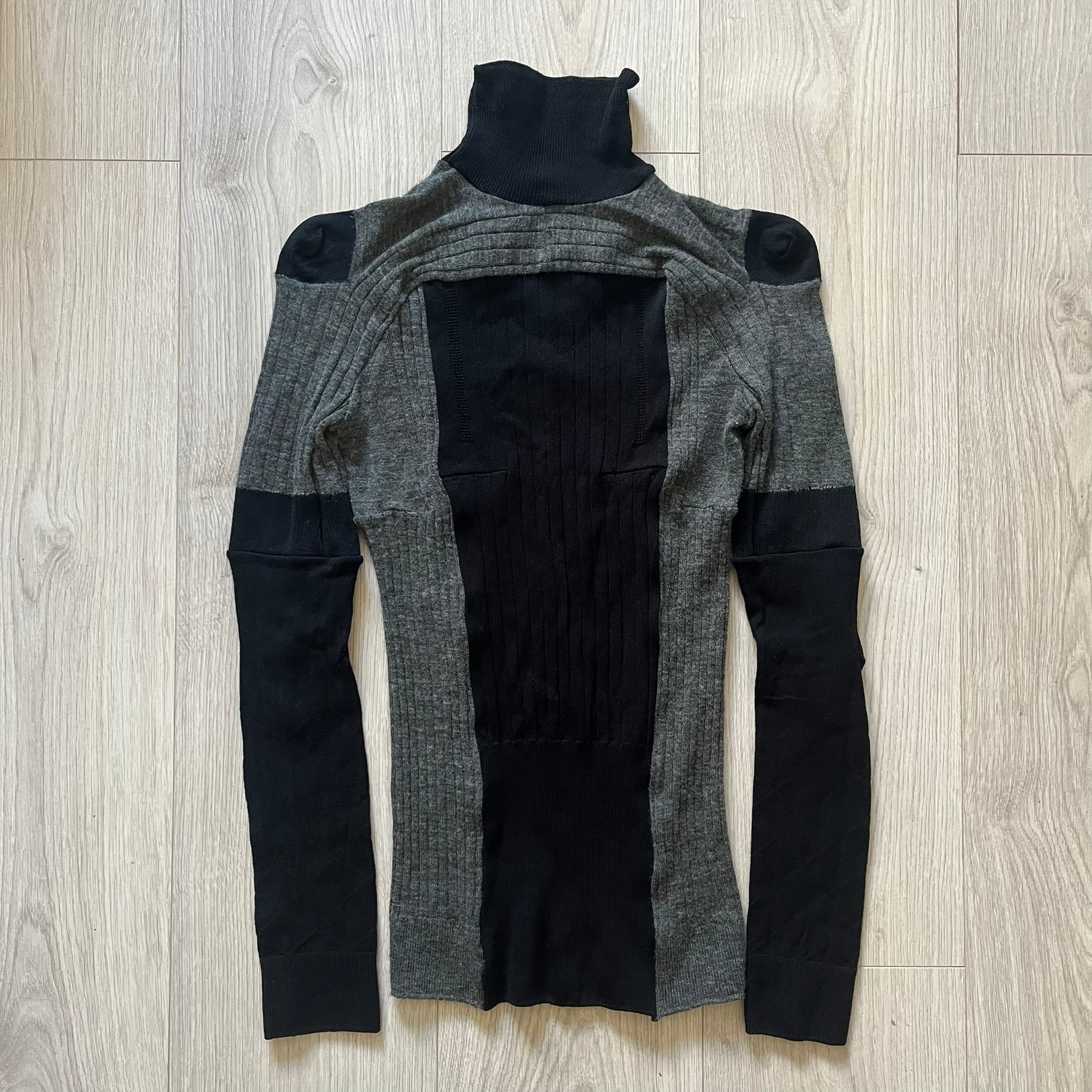 Maison Margiela x H&amp;M AW12 wool sweater in gray and black, designed with stretch fabric for a snug, comfortable fit. Features sock-inspired panels with heel details on the shoulders and elbows, a turtleneck, and long sleeves. A standout piece from the 2012 collaboration, inspired by Margiela’s Fall 1989 collection.