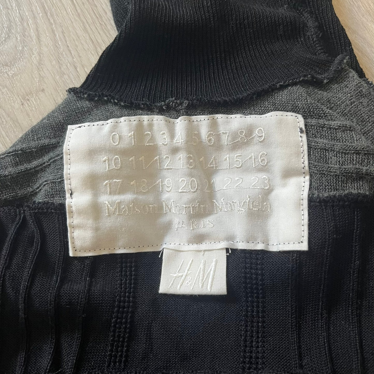 Maison Margiela x H&amp;M AW12 wool sweater in gray and black, designed with stretch fabric for a snug, comfortable fit. Features sock-inspired panels with heel details on the shoulders and elbows, a turtleneck, and long sleeves. A standout piece from the 2012 collaboration, inspired by Margiela’s Fall 1989 collection.