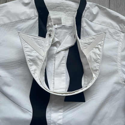 White long-sleeve shirt from the Maison Margiela x H&amp;M Autumn/Winter 2012 collaboration, constructed from 100% cotton. The design features a permanently sewn-in black bow tie positioned loosely at the collar, creating a trompe l’oeil effect that gives the appearance of a casually undone formal look. Additional details include black side panels and underarm stripes for contrast, as well as a detachable collar.