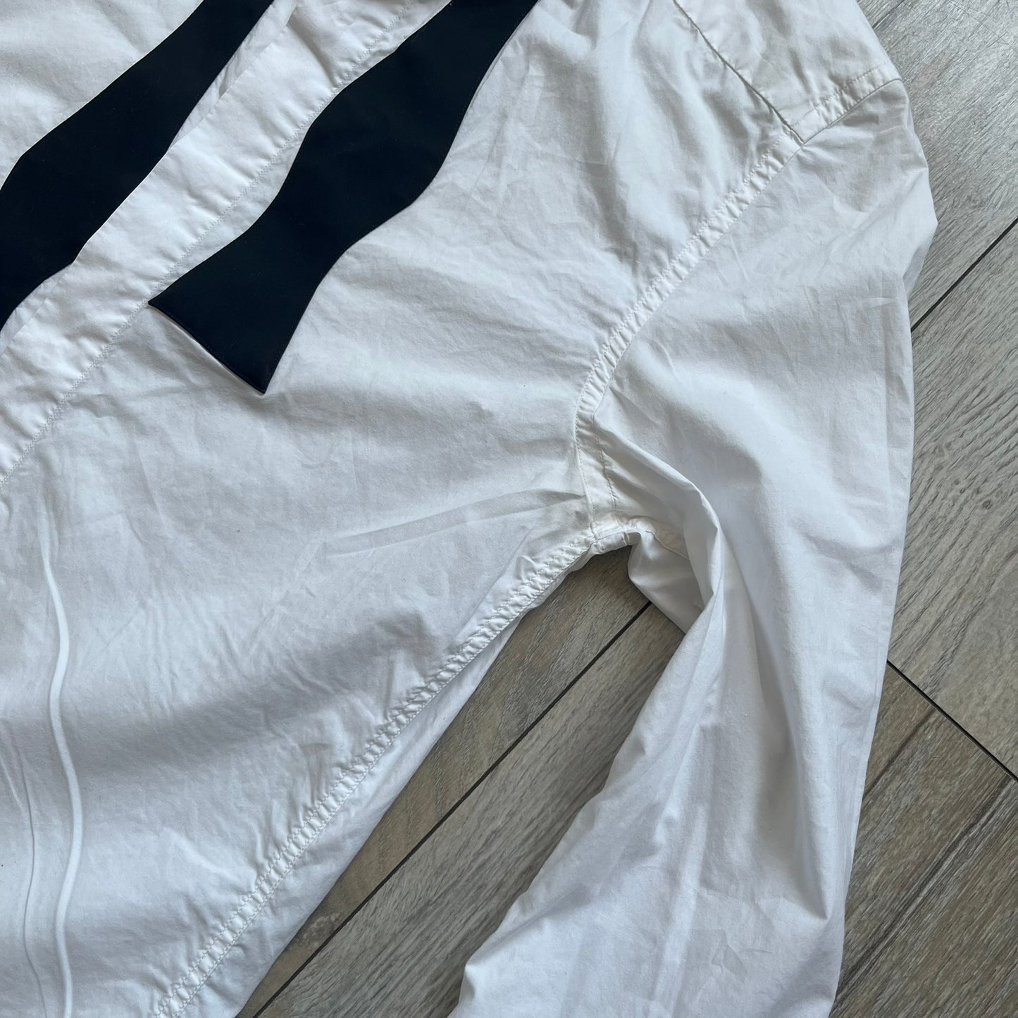 White long-sleeve shirt from the Maison Margiela x H&amp;M Autumn/Winter 2012 collaboration, constructed from 100% cotton. The design features a permanently sewn-in black bow tie positioned loosely at the collar, creating a trompe l’oeil effect that gives the appearance of a casually undone formal look.&nbsp;