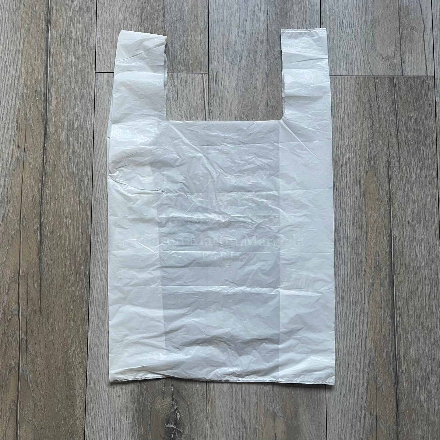 Clear/white plastic bag from the Maison Margiela x H&amp;M collaboration, designed with a cut-off bottom that allows it to be worn as a top or tank. Features big Maison Margiela x H&amp;M logos printed on the front, visible through the semi-transparent material.