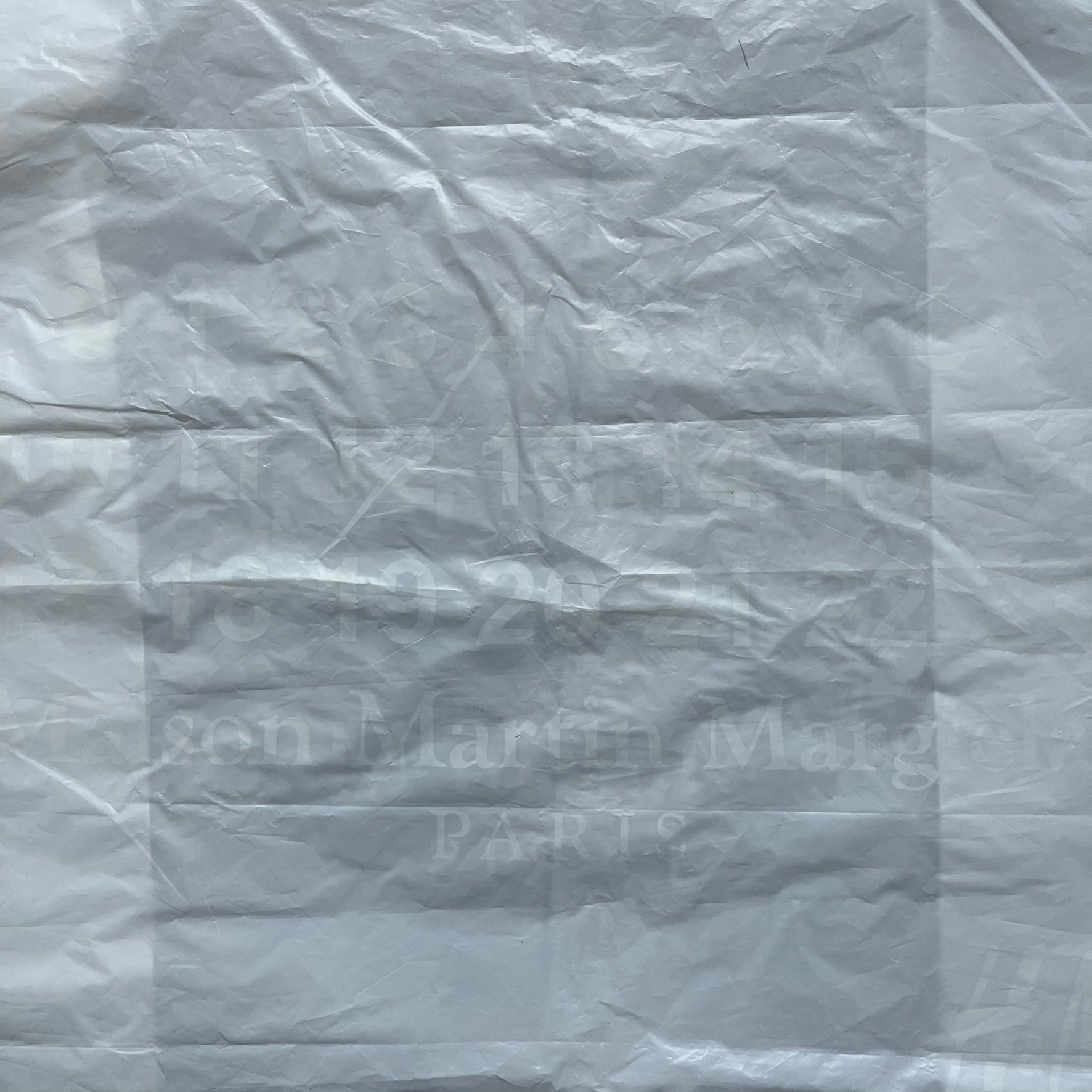 Clear/white plastic bag from the Maison Margiela x H&amp;M collaboration, designed with a cut-off bottom that allows it to be worn as a top or tank. Features big Maison Margiela x H&amp;M logos printed on the front, visible through the semi-transparent material.