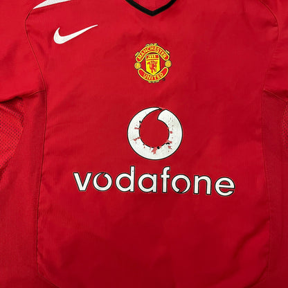 Manchester United 2004/06 Home Football T-Shirt in red, made from Nike Dri-FIT performance fabric. Features the white Vodafone sponsor logo printed across the chest, with an embroidered Manchester United crest above and a white embroidered Nike Swoosh on the right chest. Finished with white contrast detailing around the collar and sleeve hems, matching the official home design used during the 2004–2006 seasons.