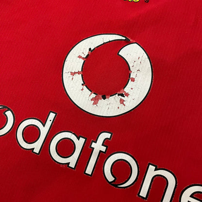 Manchester United 2004/06 Home Football T-Shirt in red, made from Nike Dri-FIT performance fabric. Features the white Vodafone sponsor logo printed across the chest, with an embroidered Manchester United crest above and a white embroidered Nike Swoosh on the right chest. Finished with white contrast detailing around the collar and sleeve hems, matching the official home design used during the 2004–2006 seasons.