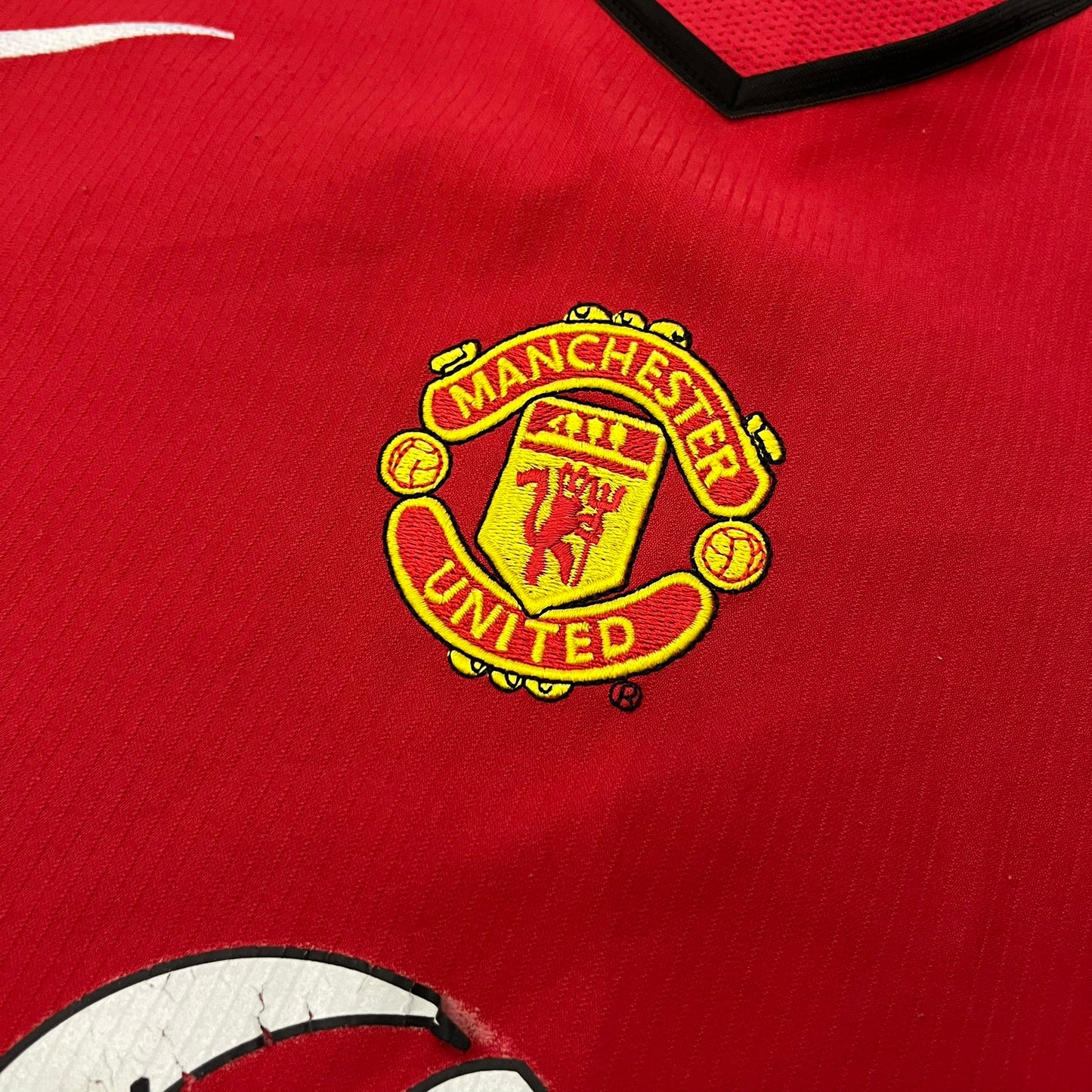 Manchester United 2004/06 Home Football T-Shirt in red, made from Nike Dri-FIT performance fabric. Features the white Vodafone sponsor logo printed across the chest, with an embroidered Manchester United crest above and a white embroidered Nike Swoosh on the right chest. Finished with white contrast detailing around the collar and sleeve hems, matching the official home design used during the 2004–2006 seasons.