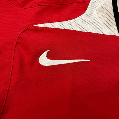 Manchester United 2004/06 Home Football T-Shirt in red, made from Nike Dri-FIT performance fabric. Features the white Vodafone sponsor logo printed across the chest, with an embroidered Manchester United crest above and a white embroidered Nike Swoosh on the right chest. Finished with white contrast detailing around the collar and sleeve hems, matching the official home design used during the 2004–2006 seasons.