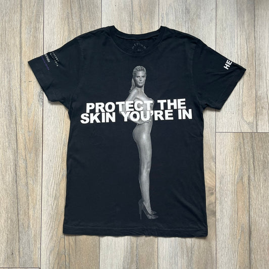 Marc Jacobs 2010s “Protect The Skin You’re In” Heidi Klum T-shirt is a black campaign tee created for skin cancer awareness. The front features an illustrative image of Heidi Klum with “Protect The Skin You’re In” text integrated into the design. The sleeves include references to “In loving memory of Dr Jessie Rubin” and support for NYU Medical Center Cancer Institute. The back displays a large “Thank You” message listing contributors to the campaign.