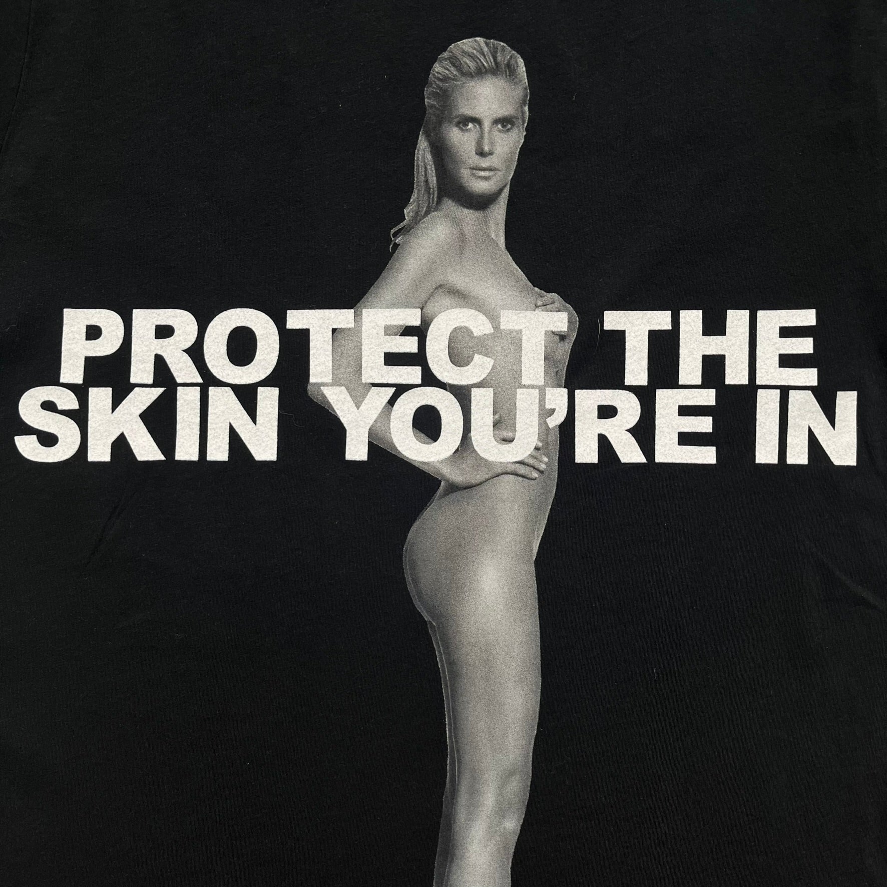 Marc Jacobs 2010s “Protect The Skin You’re In” Heidi Klum T-shirt is a black campaign tee created for skin cancer awareness. The front features an illustrative image of Heidi Klum with “Protect The Skin You’re In” text integrated into the design. The sleeves include references to “In loving memory of Dr Jessie Rubin” and support for NYU Medical Center Cancer Institute. The back displays a large “Thank You” message listing contributors to the campaign.