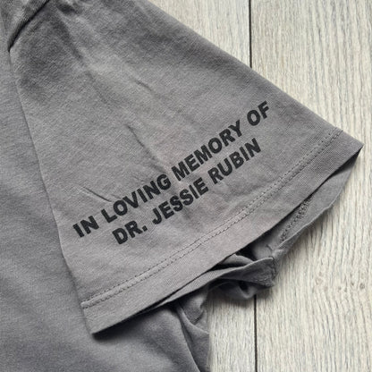 Marc Jacobs 2010s Robert Duffy Skin Cancer Awareness T-shirt is a gray campaign tee created to support skin cancer awareness. The front features an illustrative composition of Robert Duffy with Marc Jacobs included in the design. The sleeves contain printed text referencing “In loving memory of Dr Jessie Rubin” and support for NYU School of Medicine. The back includes a large “Thank You” message listing contributors involved in the campaign.

