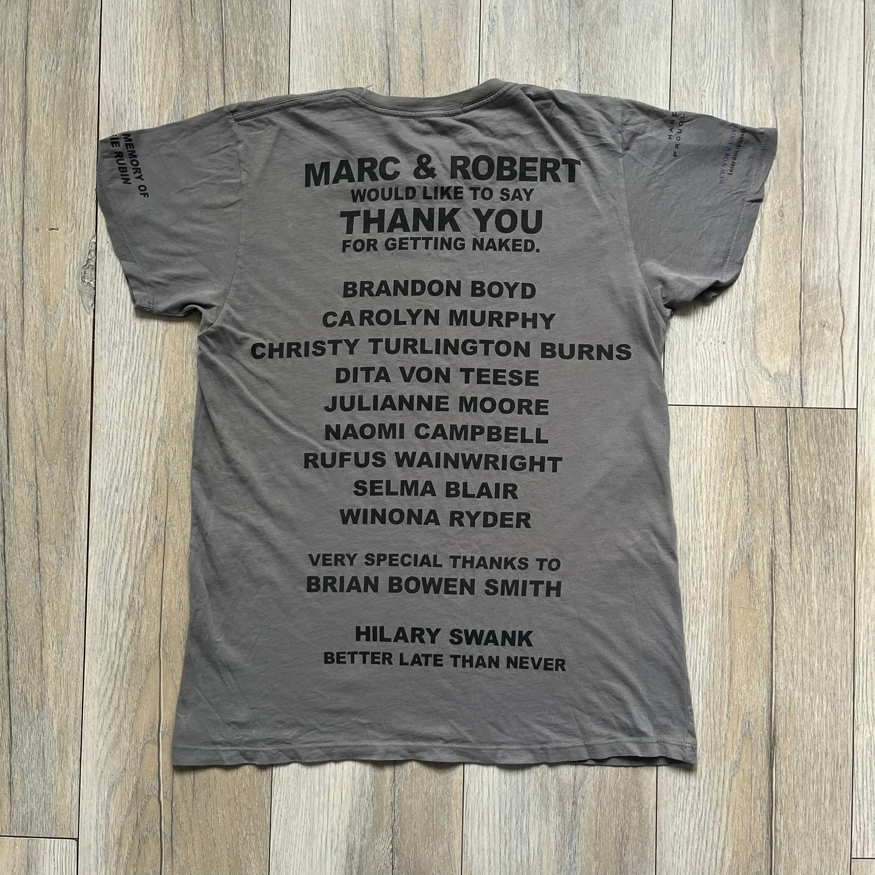 Marc Jacobs 2010s Robert Duffy Skin Cancer Awareness T-shirt is a gray campaign tee created to support skin cancer awareness. The front features an illustrative composition of Robert Duffy with Marc Jacobs included in the design. The sleeves contain printed text referencing “In loving memory of Dr Jessie Rubin” and support for NYU School of Medicine. The back includes a large “Thank You” message listing contributors involved in the campaign.
