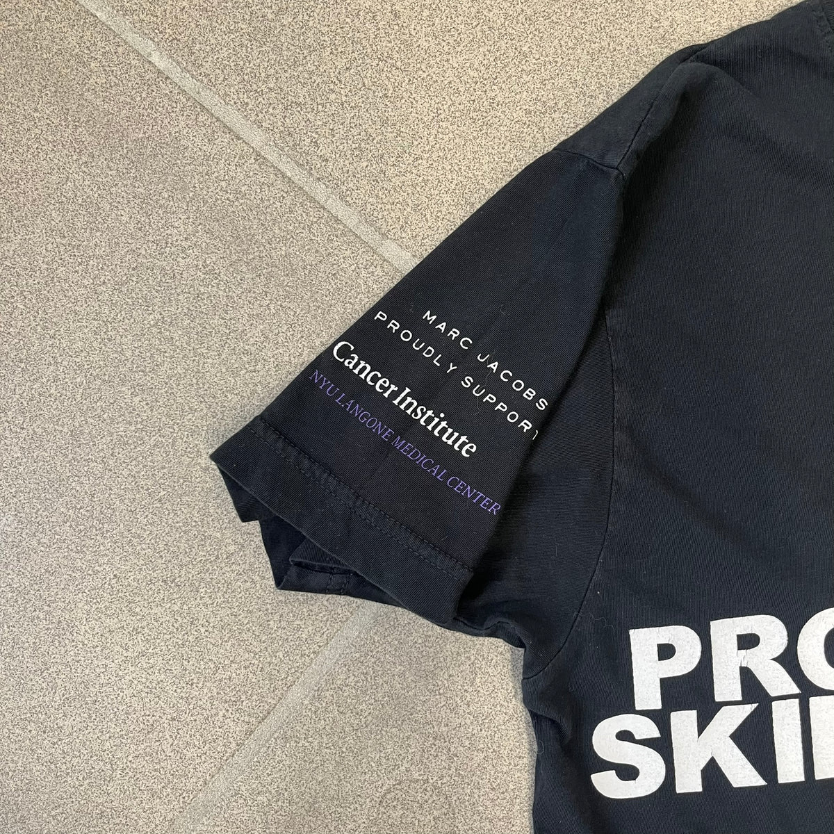 Marc Jacobs 2010s “Protect The Skin You’re In” Heidi Klum T-shirt is a black campaign tee created for skin cancer awareness. The front features an illustrative image of Heidi Klum with “Protect The Skin You’re In” text integrated into the design. The sleeves include "Heidi” and support for NYU Medical Center Cancer Institute. The back displays a large “Thank You” message listing contributors to the campaign.