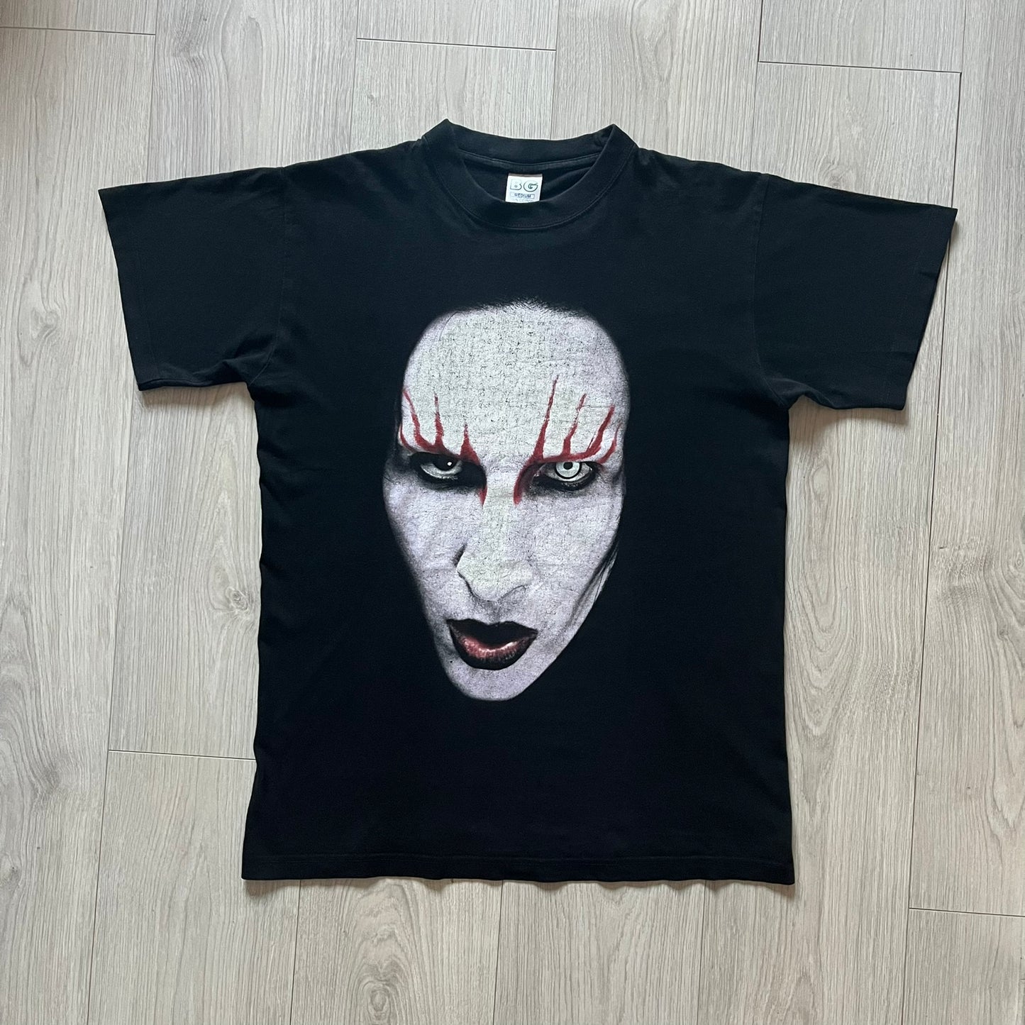 Marilyn Manson Holy Wood Face Tee from 2000, made on a black BG blank. Features a large front graphic of Manson’s face with signature white makeup, red accents, and eye contact. The back includes red Marilyn Manson text with a small 2000 Giant license, great piece from the Holy Wood era.