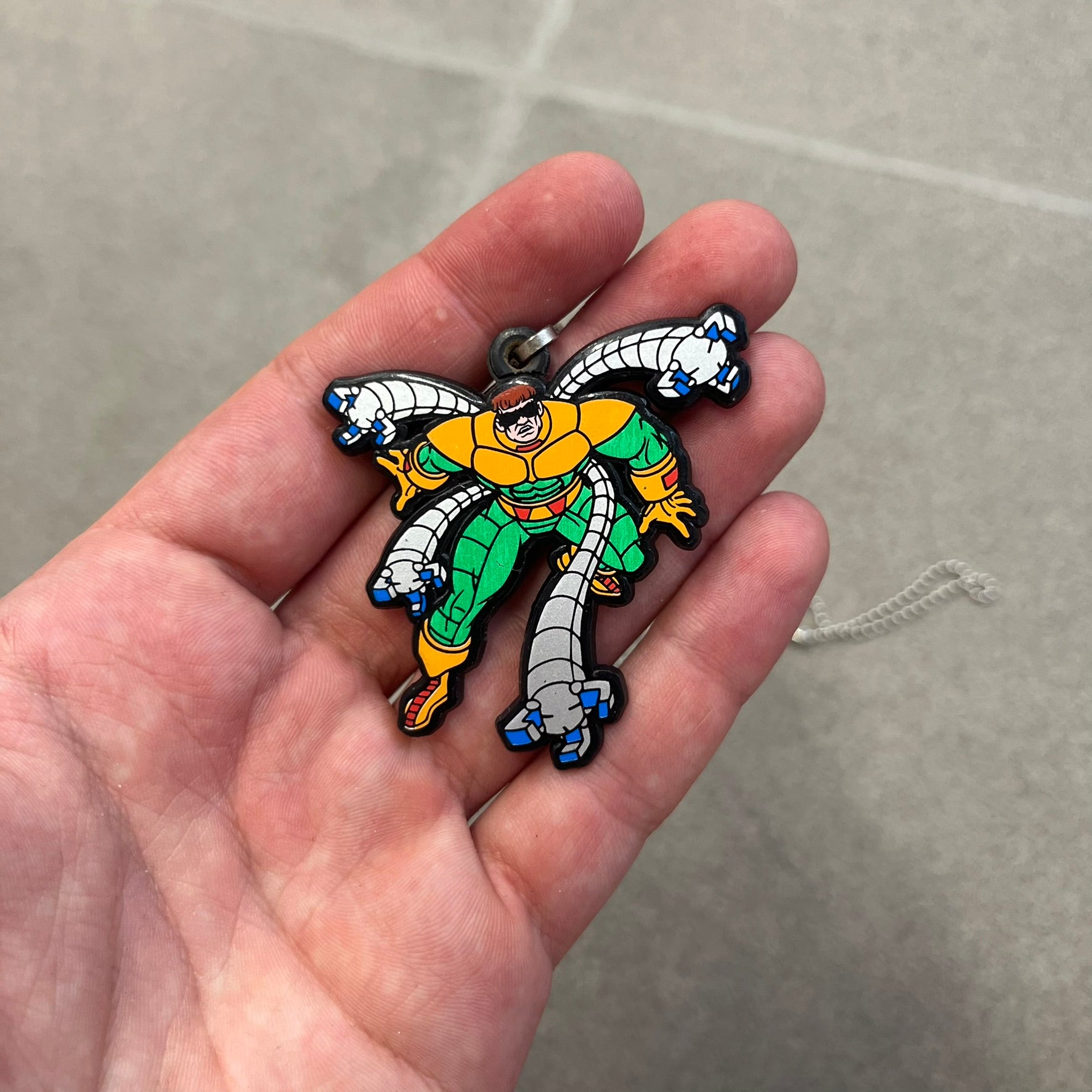 Marvel 1995 Doctor Octopus Necklace features a 2D cartoon-style Doctor Octopus pendant with a colorful graphic on the front. The back of the pendant is black and includes 1995 Marvel licensing details. It has a metal loop at the top and comes with a basic steel chain.
