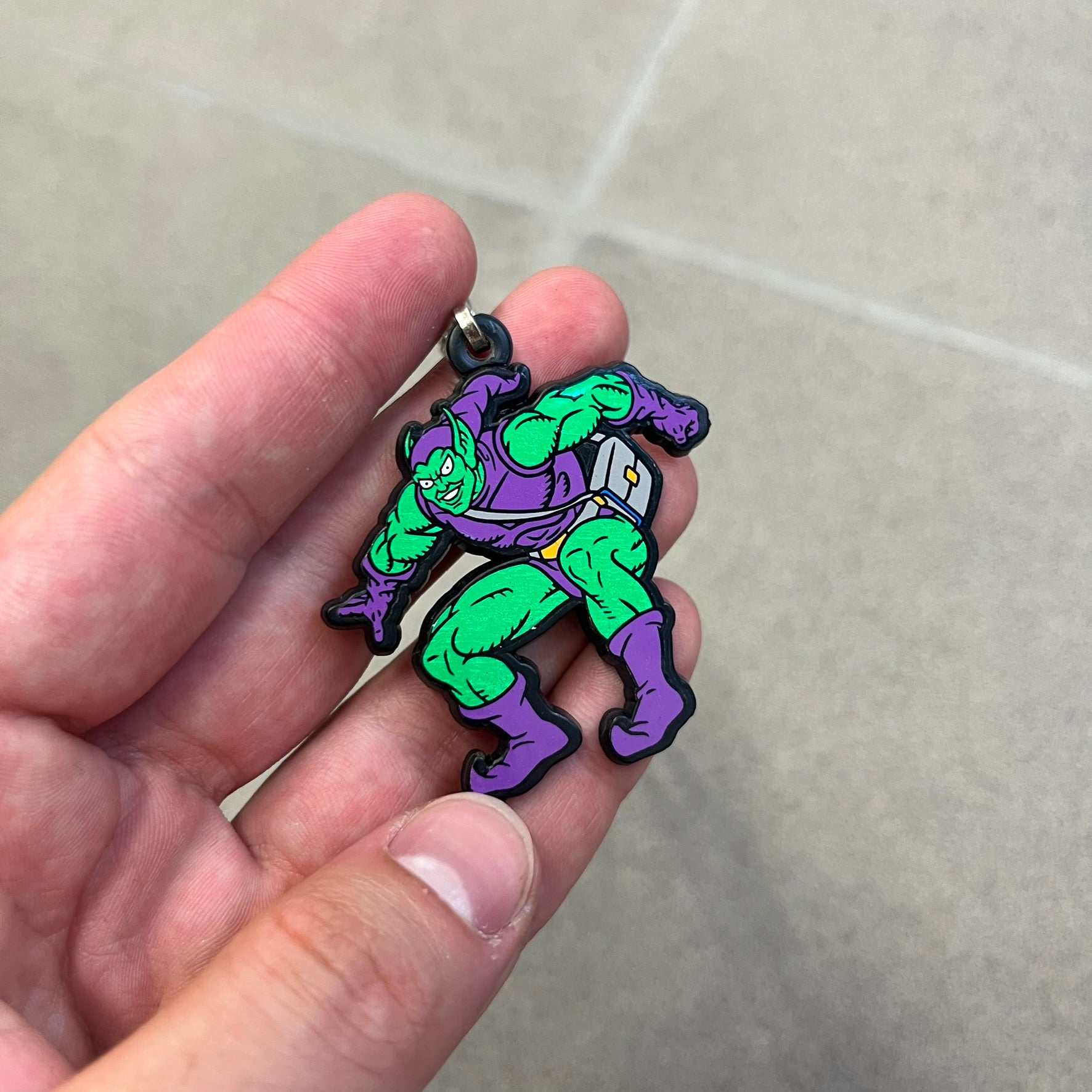 Marvel 1995 Green Goblin Necklace features a 2D cartoon-style Green Goblin pendant with a colorful graphic on the front. The back of the pendant is black and includes 1995 Marvel licensing details. It has a metal loop at the top and comes with a basic steel chain.