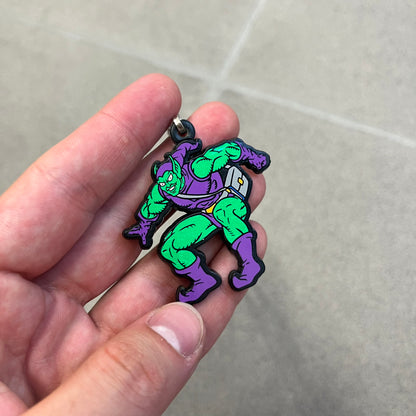 Marvel 1995 Green Goblin Necklace features a 2D cartoon-style Green Goblin pendant with a colorful graphic on the front. The back of the pendant is black and includes 1995 Marvel licensing details. It has a metal loop at the top and comes with a basic steel chain.