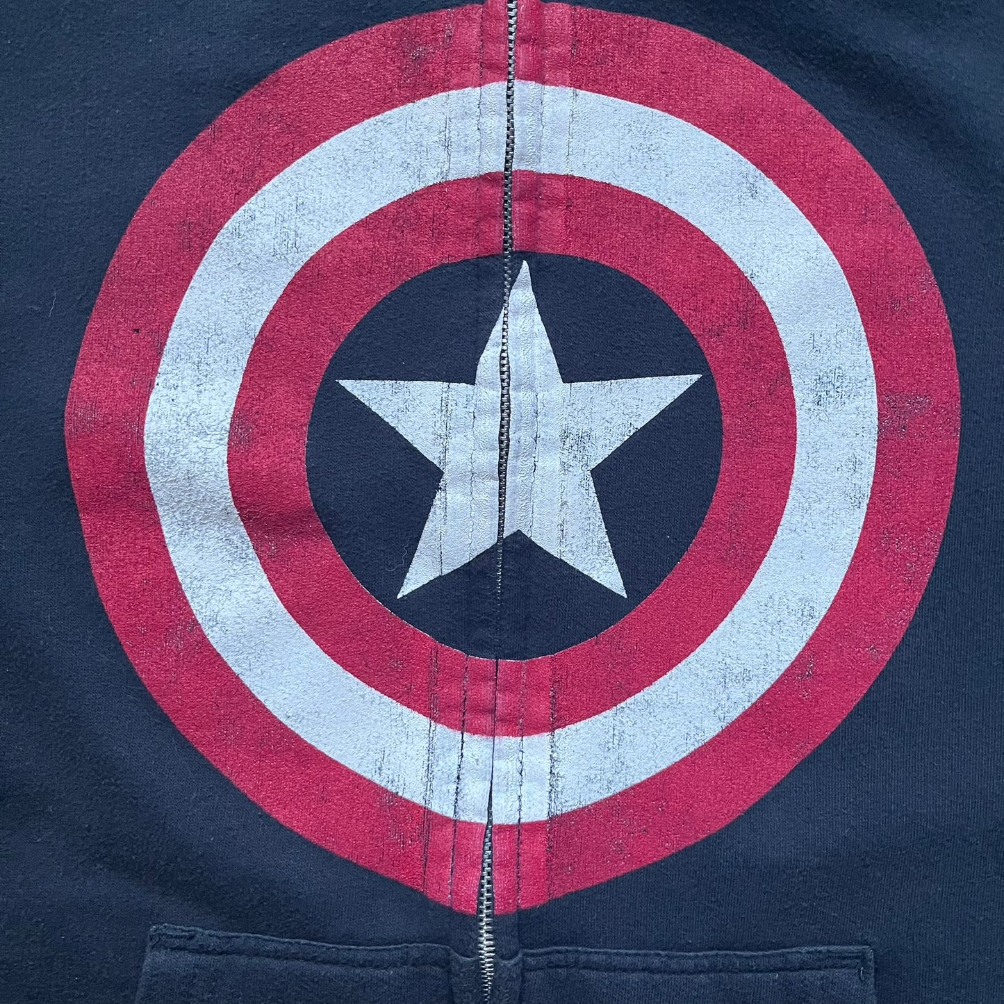 Black hoodie with a large Captain America shield graphic on the front. Made from an 80/20 polyester blend, lightweight. Features metal zipper, front pockets, and WeLoveFine × Marvel neck tag. The shield graphic has an intentional rough texture.