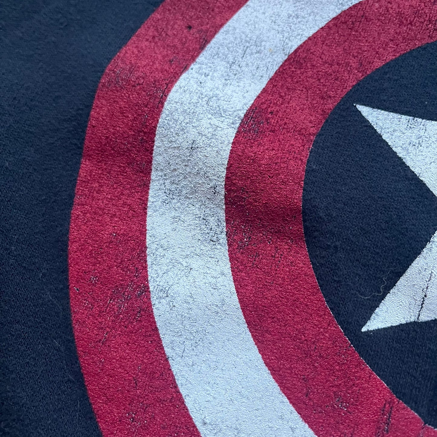 Black hoodie with a large Captain America shield graphic on the front. Made from an 80/20 polyester blend, lightweight. Features metal zipper, front pockets, and WeLoveFine × Marvel neck tag. The shield graphic has an intentional rough texture.