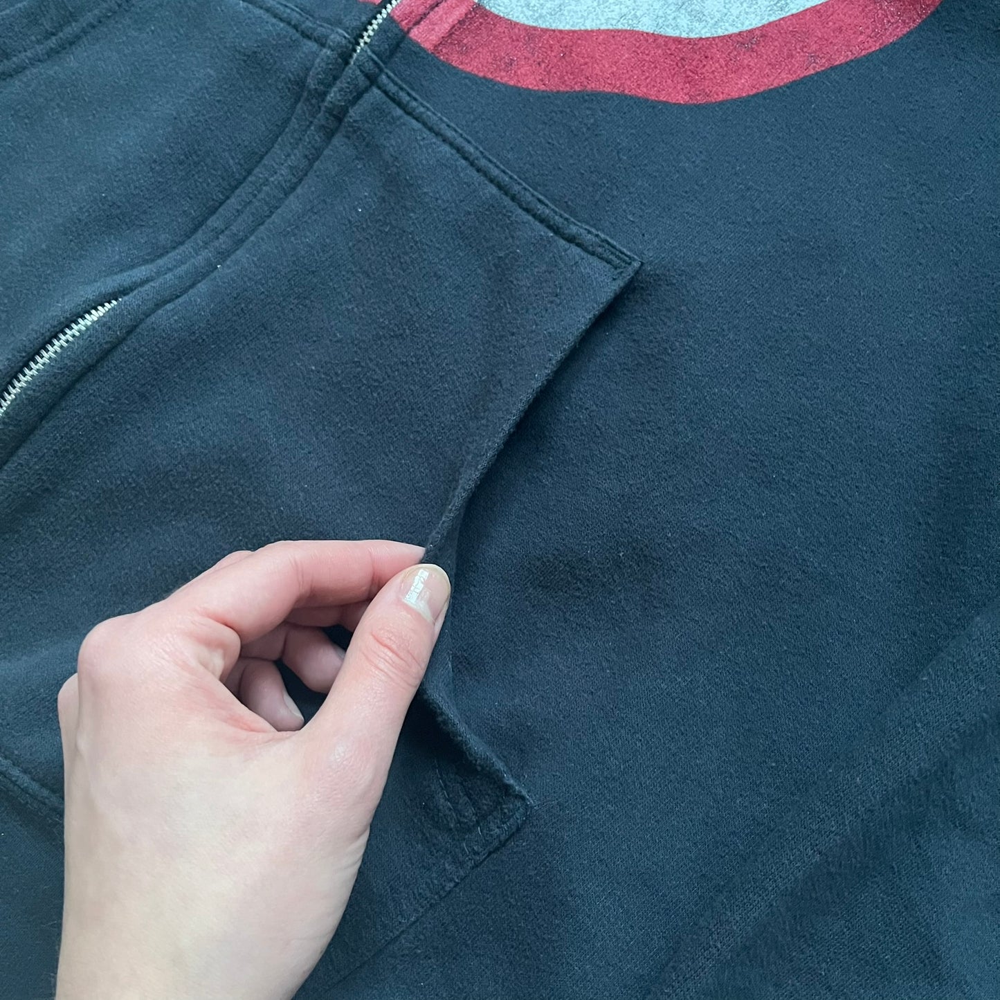 Black hoodie with a large Captain America shield graphic on the front. Made from an 80/20 polyester blend, lightweight. Features metal zipper, front pockets, and WeLoveFine × Marvel neck tag. The shield graphic has an intentional rough texture.