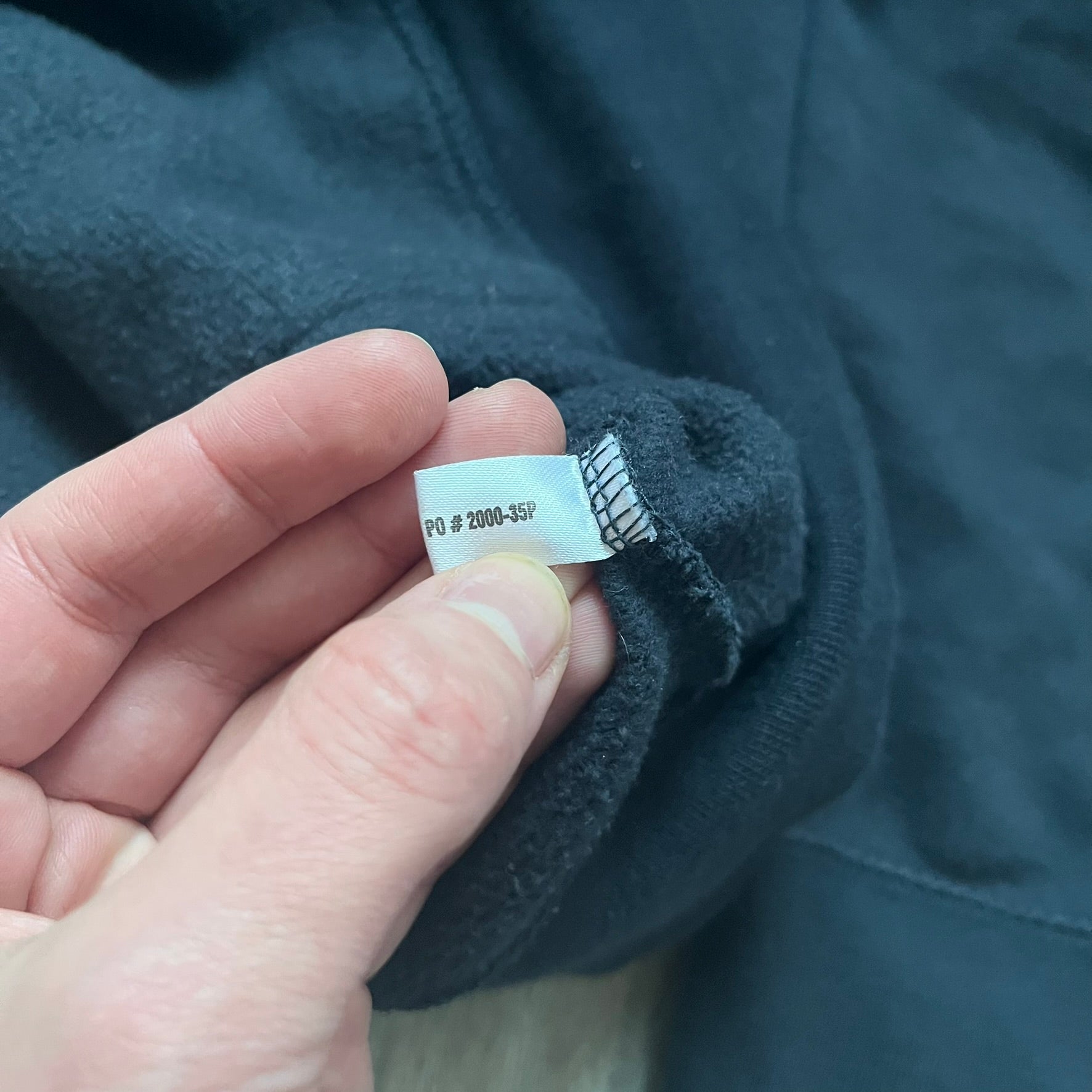 Black hoodie with a large Captain America shield graphic on the front. Made from an 80/20 polyester blend, lightweight. Features metal zipper, front pockets, and WeLoveFine × Marvel neck tag. The shield graphic has an intentional rough texture.