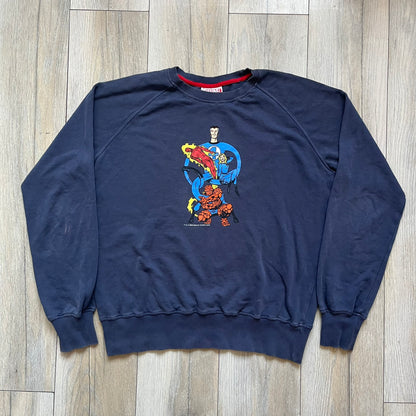 Marvel Fantastic Four 2003 Navy Crewneck is a navy sweatshirt made from 100% cotton with an official Marvel neck tag. The front features a central graphic of the Fantastic Four characters intertwined together, with Reed Richards in a stretched form, Human Torch flying above, Ben Grimm holding Reed, and Sue Storm positioned within the composition. Small white licensing text with the 2003 date appears beneath the graphic.