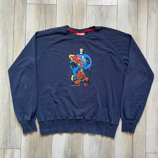 Marvel Fantastic Four 2003 Navy Crewneck is a navy sweatshirt made from 100% cotton with an official Marvel neck tag. The front features a central graphic of the Fantastic Four characters intertwined together, with Reed Richards in a stretched form, Human Torch flying above, Ben Grimm holding Reed, and Sue Storm positioned within the composition. Small white licensing text with the 2003 date appears beneath the graphic.