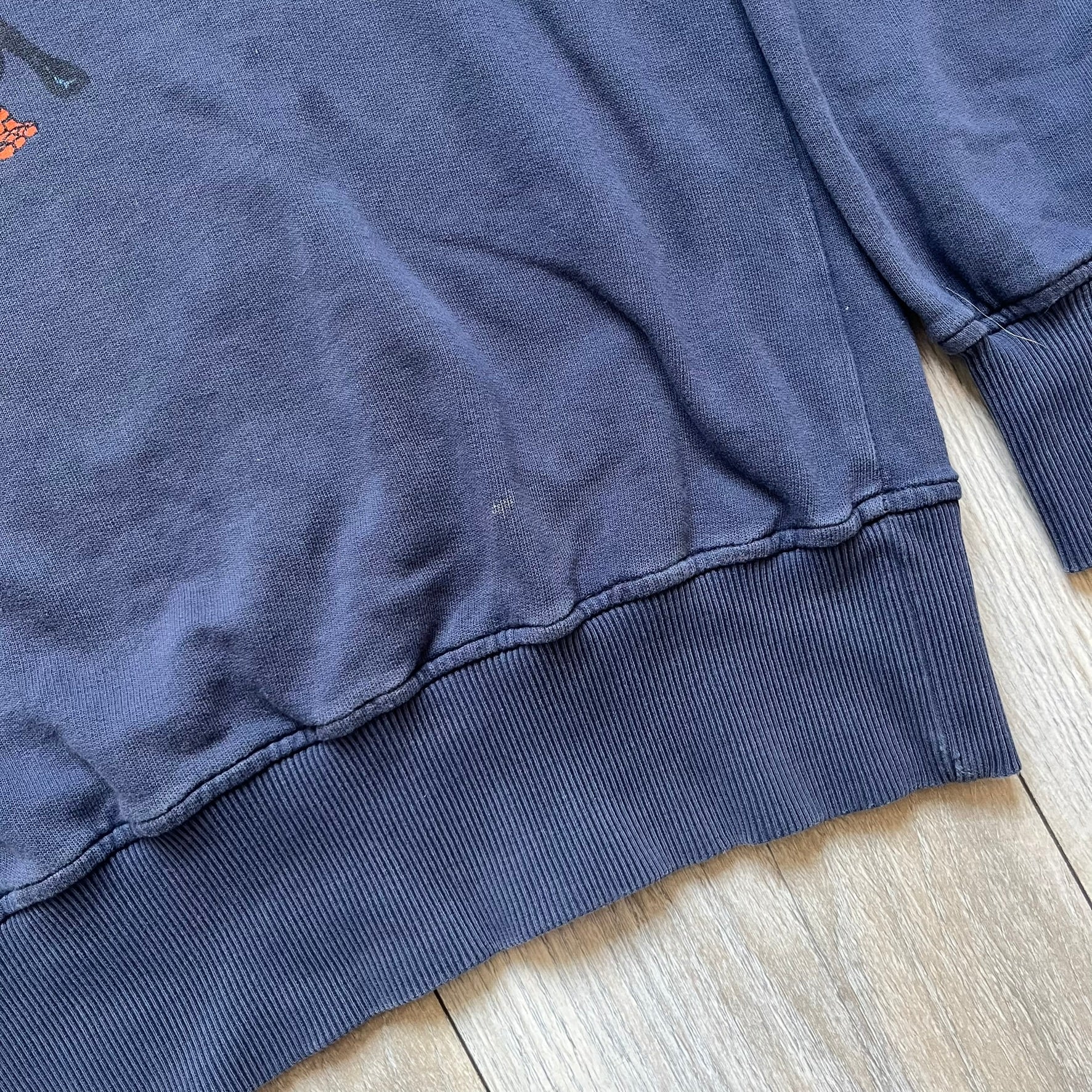 Marvel Fantastic Four 2003 Navy Crewneck is a navy sweatshirt made from 100% cotton with an official Marvel neck tag. The front features a central graphic of the Fantastic Four characters intertwined together, with Reed Richards in a stretched form, Human Torch flying above, Ben Grimm holding Reed, and Sue Storm positioned within the composition. Small white licensing text with the 2003 date appears beneath the graphic.