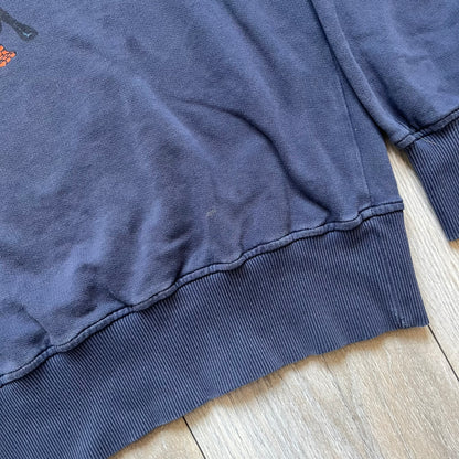 Marvel Fantastic Four 2003 Navy Crewneck is a navy sweatshirt made from 100% cotton with an official Marvel neck tag. The front features a central graphic of the Fantastic Four characters intertwined together, with Reed Richards in a stretched form, Human Torch flying above, Ben Grimm holding Reed, and Sue Storm positioned within the composition. Small white licensing text with the 2003 date appears beneath the graphic.