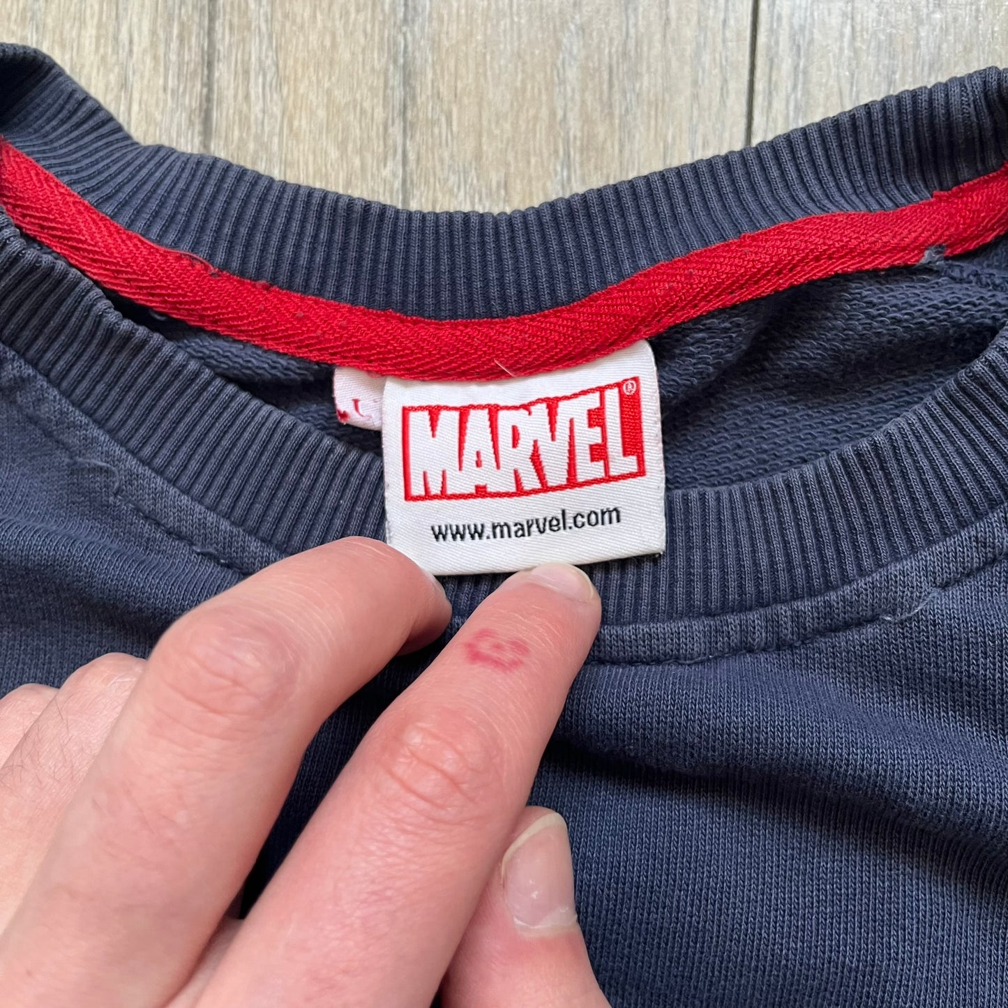 Marvel Fantastic Four 2003 Navy Crewneck is a navy sweatshirt made from 100% cotton with an official Marvel neck tag. The front features a central graphic of the Fantastic Four characters intertwined together, with Reed Richards in a stretched form, Human Torch flying above, Ben Grimm holding Reed, and Sue Storm positioned within the composition. Small white licensing text with the 2003 date appears beneath the graphic.