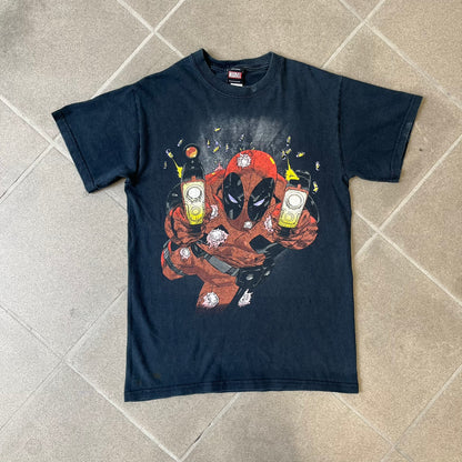 Marvel Mad Engine 2000's Deadpool Tee features a black T-shirt made by Mad Engine. The front has a comic-style graphic of Deadpool in mid-air firing two pistols, with bullets and bullet holes shown throughout the design.
