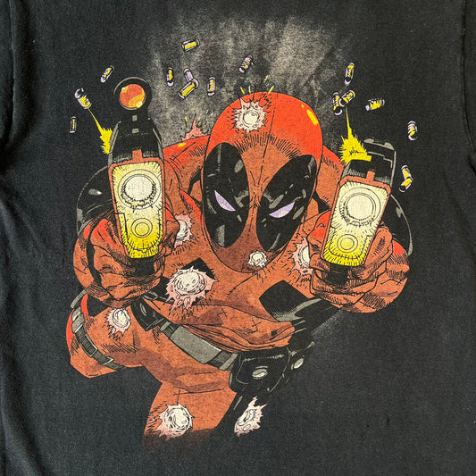 Marvel Mad Engine 2000's Deadpool Tee features a black T-shirt made by Mad Engine. The front has a comic-style graphic of Deadpool in mid-air firing two pistols, with bullets and bullet holes shown throughout the design.
