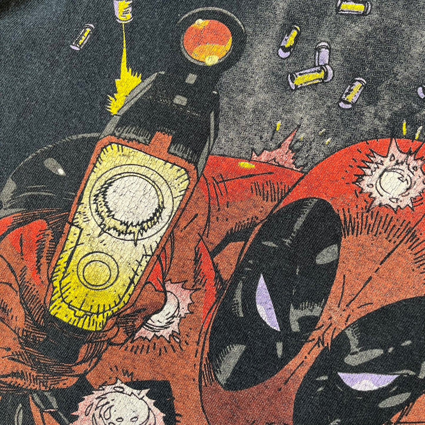 Marvel Mad Engine 2000's Deadpool Tee features a black T-shirt made by Mad Engine. The front has a comic-style graphic of Deadpool in mid-air firing two pistols, with bullets and bullet holes shown throughout the design.
