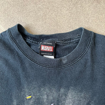 Marvel Mad Engine 2000's Deadpool Tee features a black T-shirt made by Mad Engine. The front has a comic-style graphic of Deadpool in mid-air firing two pistols, with bullets and bullet holes shown throughout the design.
