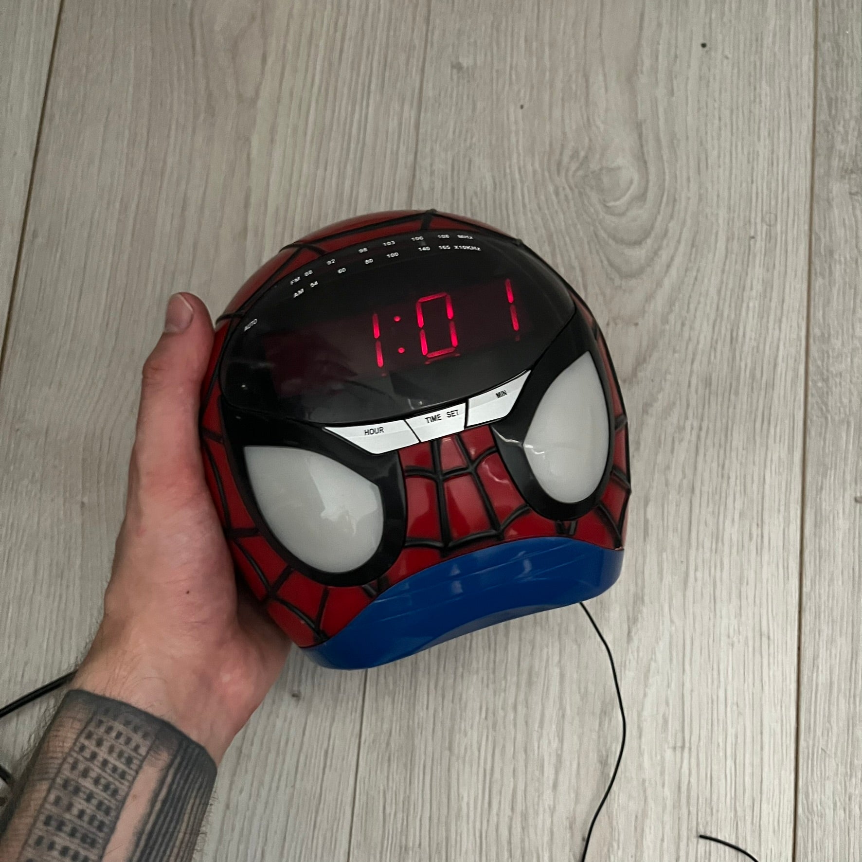 Marvel Spider-Man 2006 AM/FM Alarm Clock Radio is a digital alarm clock shaped like Spider-Man’s head with a multicolor design. It features AM/FM radio functionality and a built-in red projection display that projects the time onto a nearby surface. The clock operates using a standard 110V two-prong power connection or a 9V backup battery. All functions are fully working.
