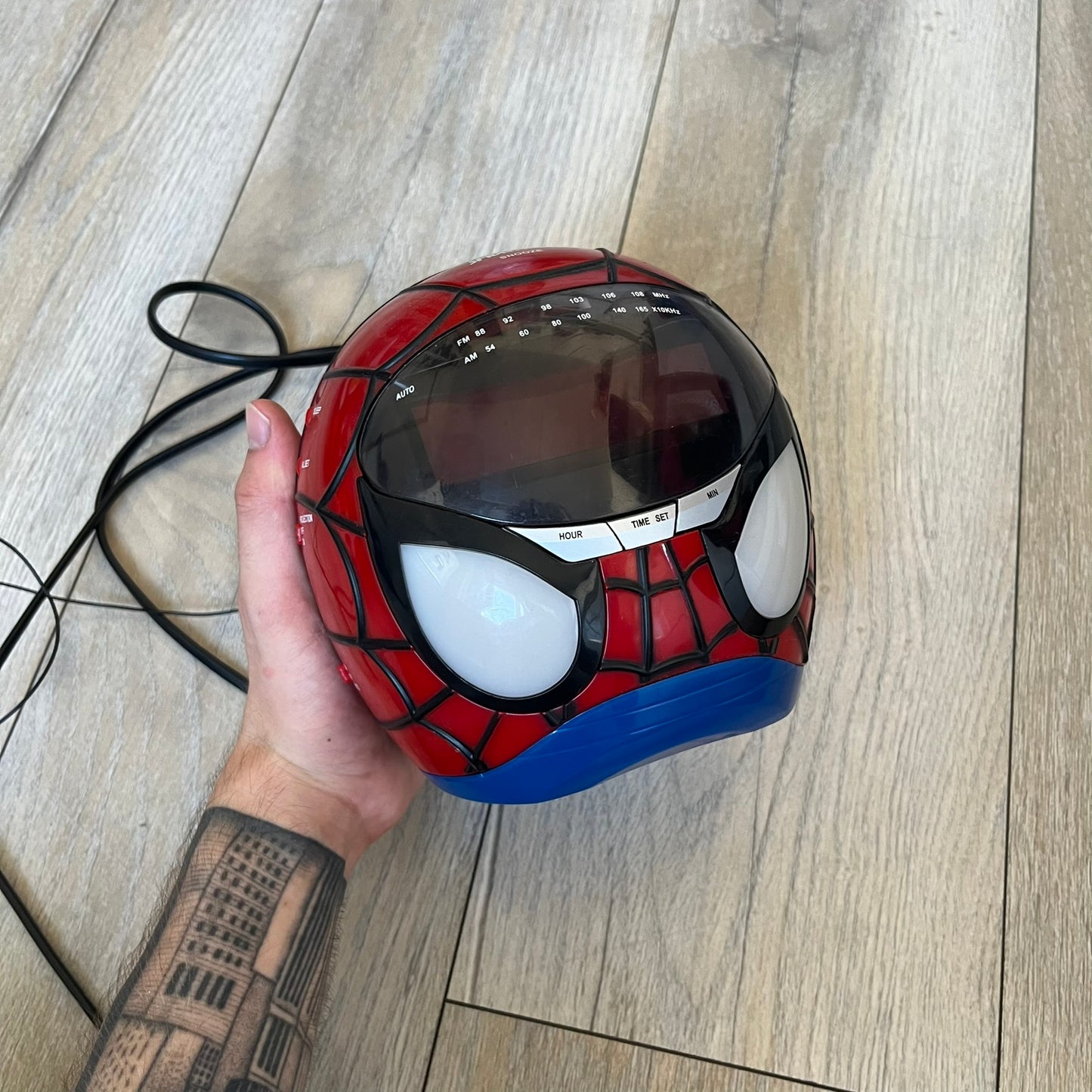 Marvel Spider-Man 2006 AM/FM Alarm Clock Radio is a digital alarm clock shaped like Spider-Man’s head with a multicolor design. It features AM/FM radio functionality and a built-in red projection display that projects the time onto a nearby surface. The clock operates using a standard 110V two-prong power connection or a 9V backup battery. All functions are fully working.
