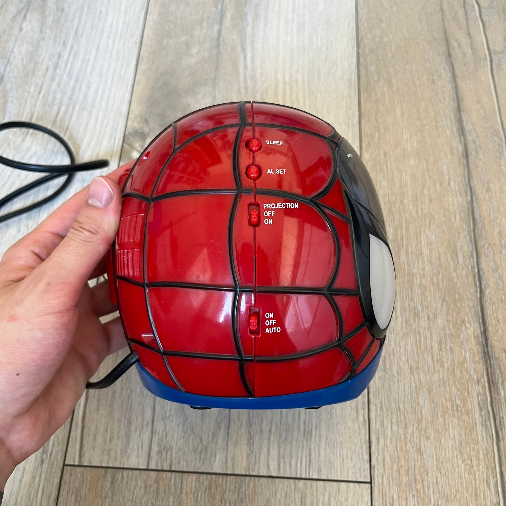 Marvel Spider-Man 2006 AM/FM Alarm Clock Radio is a digital alarm clock shaped like Spider-Man’s head with a multicolor design. It features AM/FM radio functionality and a built-in red projection display that projects the time onto a nearby surface. The clock operates using a standard 110V two-prong power connection or a 9V backup battery. All functions are fully working.
