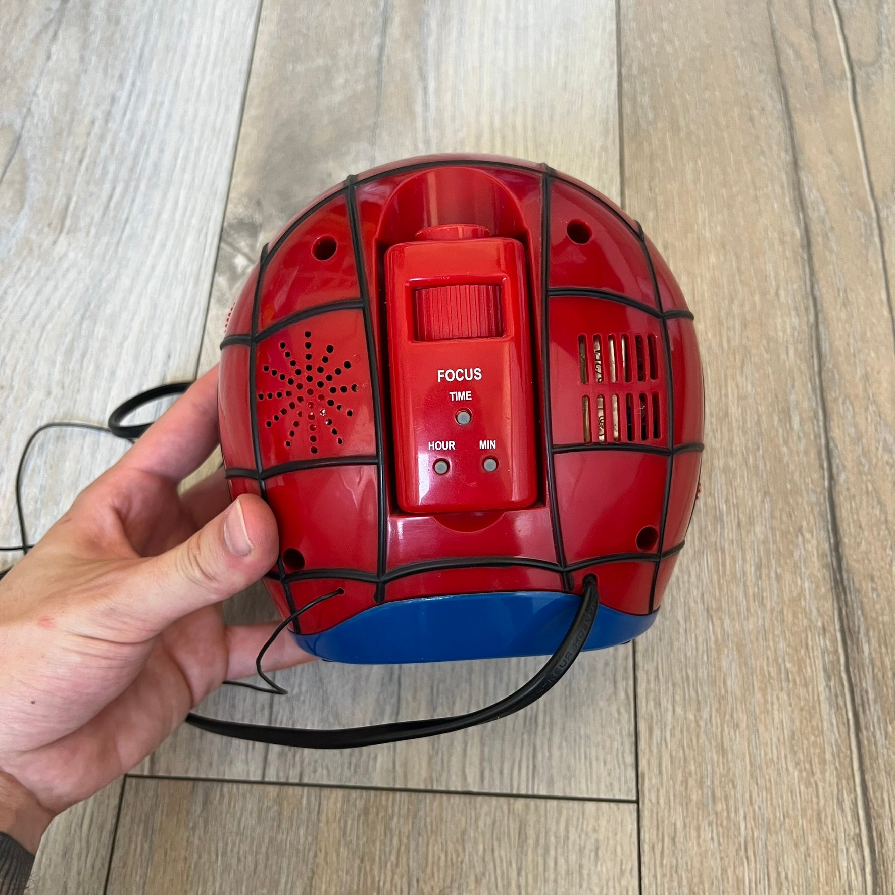 Marvel Spider-Man 2006 AM/FM Alarm Clock Radio is a digital alarm clock shaped like Spider-Man’s head with a multicolor design. It features AM/FM radio functionality and a built-in red projection display that projects the time onto a nearby surface. The clock operates using a standard 110V two-prong power connection or a 9V backup battery. All functions are fully working.
