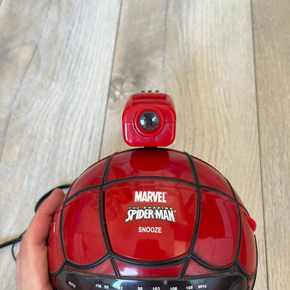 Marvel Spider-Man 2006 AM/FM Alarm Clock Radio is a digital alarm clock shaped like Spider-Man’s head with a multicolor design. It features AM/FM radio functionality and a built-in red projection display that projects the time onto a nearby surface. The clock operates using a standard 110V two-prong power connection or a 9V backup battery. All functions are fully working.

