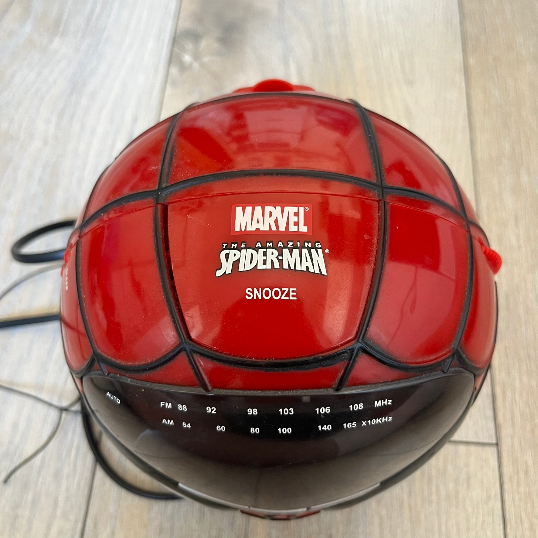 Marvel Spider-Man 2006 AM/FM Alarm Clock Radio is a digital alarm clock shaped like Spider-Man’s head with a multicolor design. It features AM/FM radio functionality and a built-in red projection display that projects the time onto a nearby surface. The clock operates using a standard 110V two-prong power connection or a 9V backup battery. All functions are fully working.
