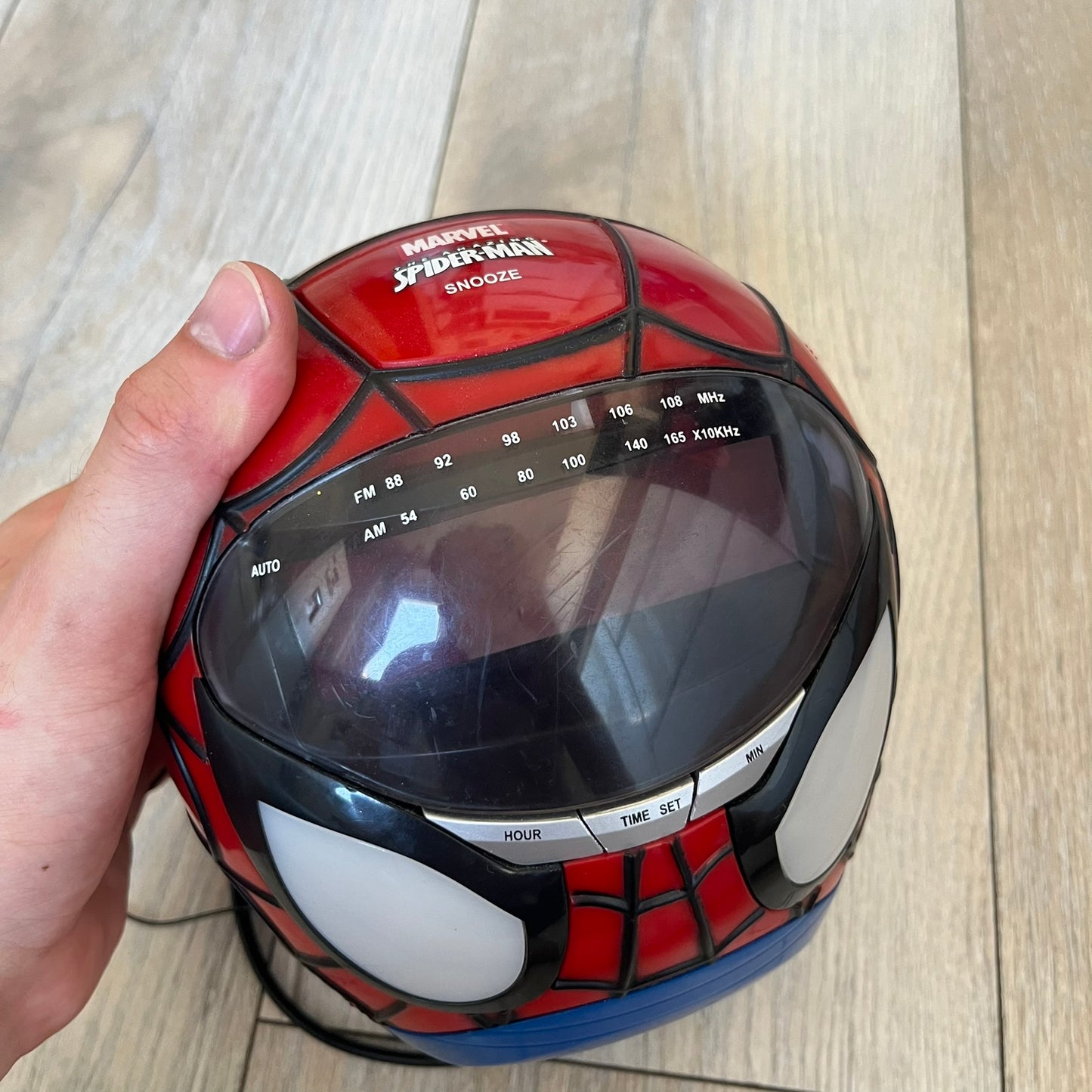Marvel Spider-Man 2006 AM/FM Alarm Clock Radio is a digital alarm clock shaped like Spider-Man’s head with a multicolor design. It features AM/FM radio functionality and a built-in red projection display that projects the time onto a nearby surface. The clock operates using a standard 110V two-prong power connection or a 9V backup battery. All functions are fully working.
