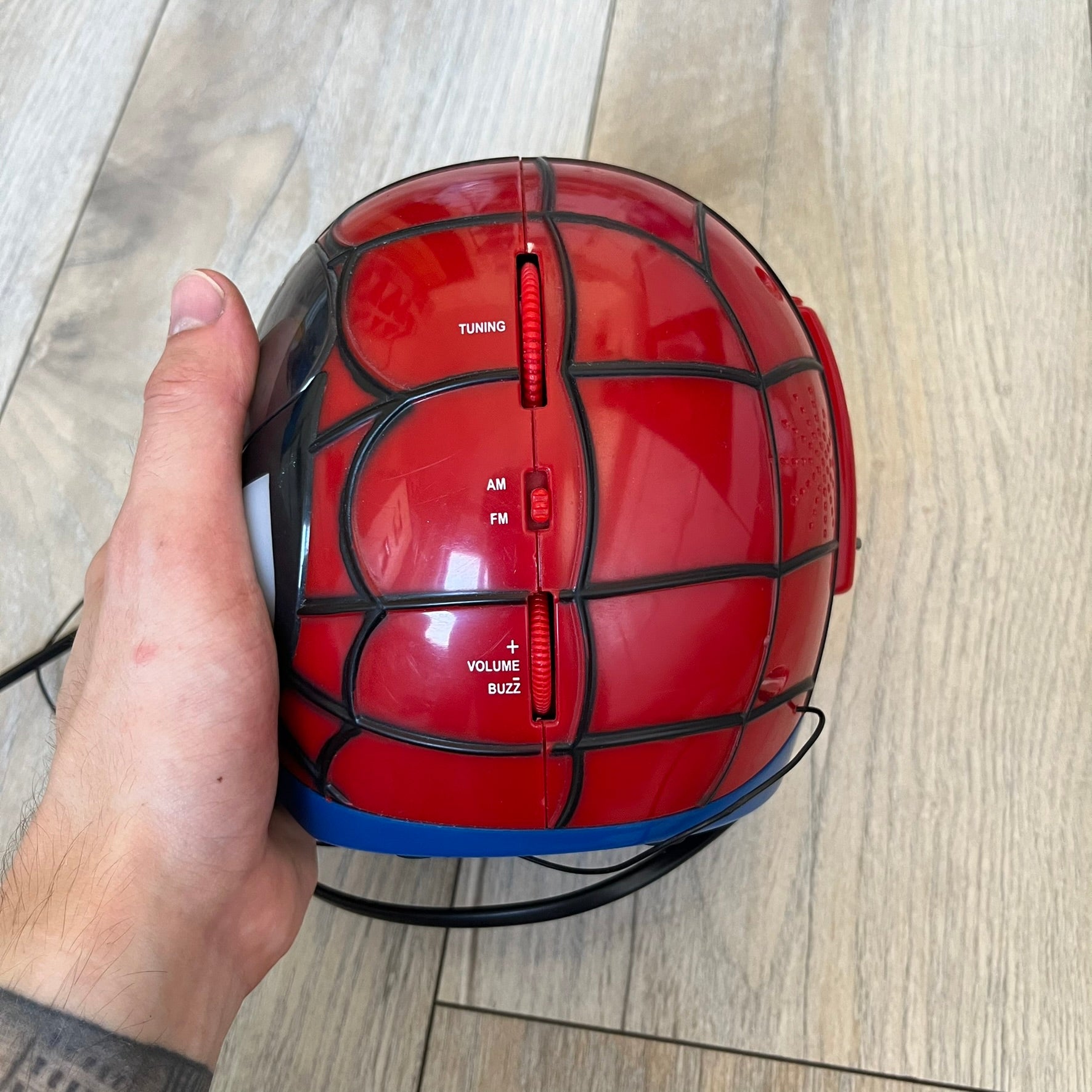 Marvel Spider-Man 2006 AM/FM Alarm Clock Radio is a digital alarm clock shaped like Spider-Man’s head with a multicolor design. It features AM/FM radio functionality and a built-in red projection display that projects the time onto a nearby surface. The clock operates using a standard 110V two-prong power connection or a 9V backup battery. All functions are fully working.
