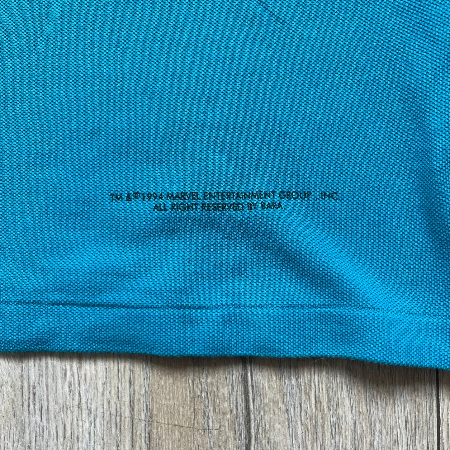 Marvel Comics Spider-Man 1994 Blue Embroidered Polo is a blue polo shirt featuring embroidered Spider-Man branding. The left chest displays an embroidered Spider-Man graphic, while the sleeve includes yellow “Spider-Man” text embroidery. The lower front is finished with small black “1994” text, and the shirt includes a large Marvel Comics neck tag.